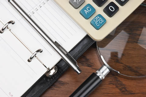 Notepad, pen, calculator, and magnifying glass on a wooden table