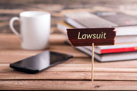 Desk that contains a stack of books, coffee mug, phone, and a small sign with text, "lawsuit"