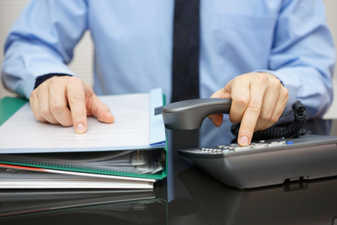 Man seated at a desk who is reviewing documentation and holding a phone